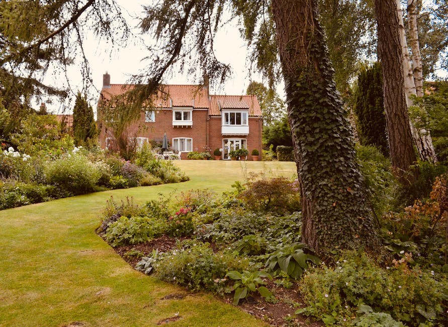 An expansive garden landscape at sunset, featuring a winding river flowing through lush green fields and clusters of mature trees. The river's gentle curves create serene borders around well-maintaine